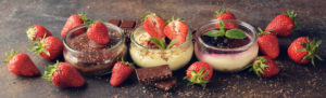 Different summer cheesecakes in jars on a brown background